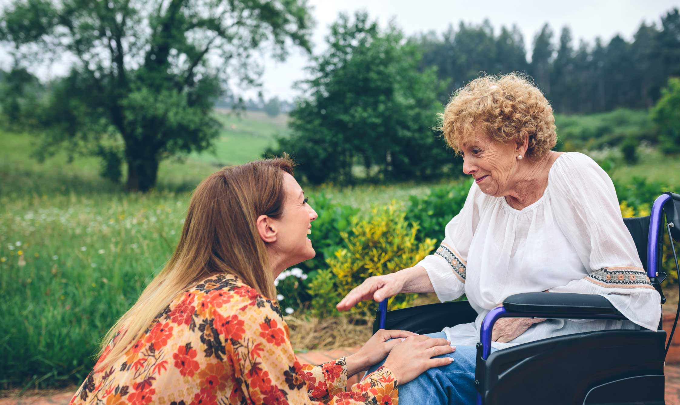 senior woman in a wheelchair laughing outside with her adult daughter