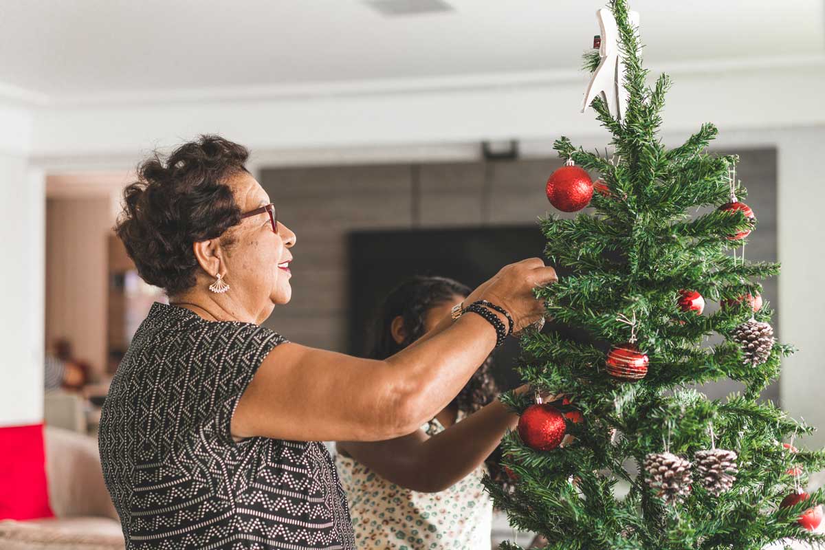 senior woman decorating a christmas tree with ornaments